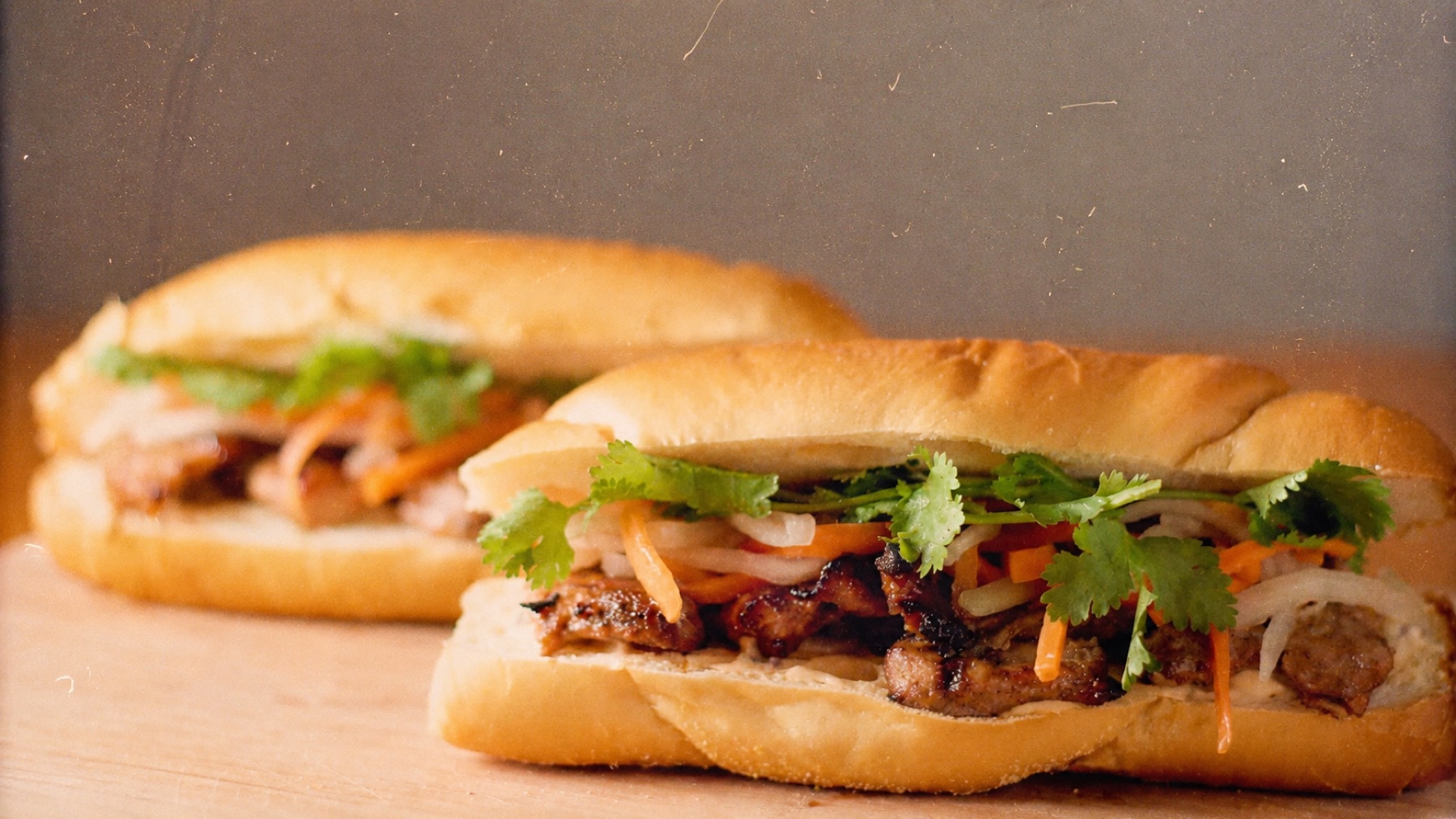 Two grilled pork bánh mì stacked on a wooden board